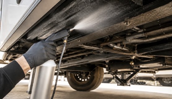 Technician spraying mouse repellent on an RV undercarriage
