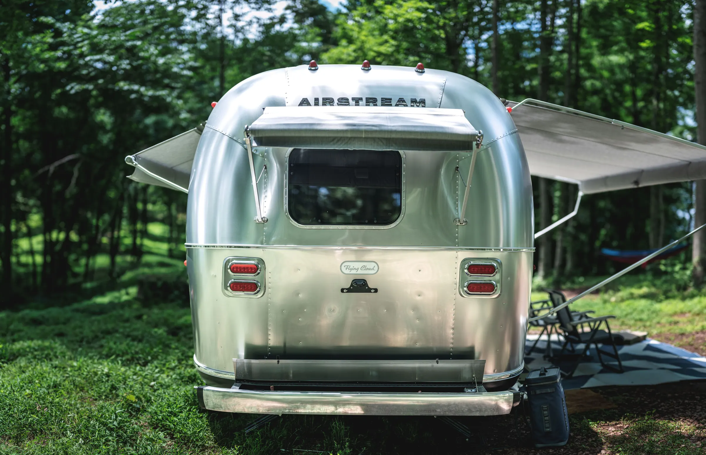 Rear of an Airstream Flying Cloud with awnings out in a green forest